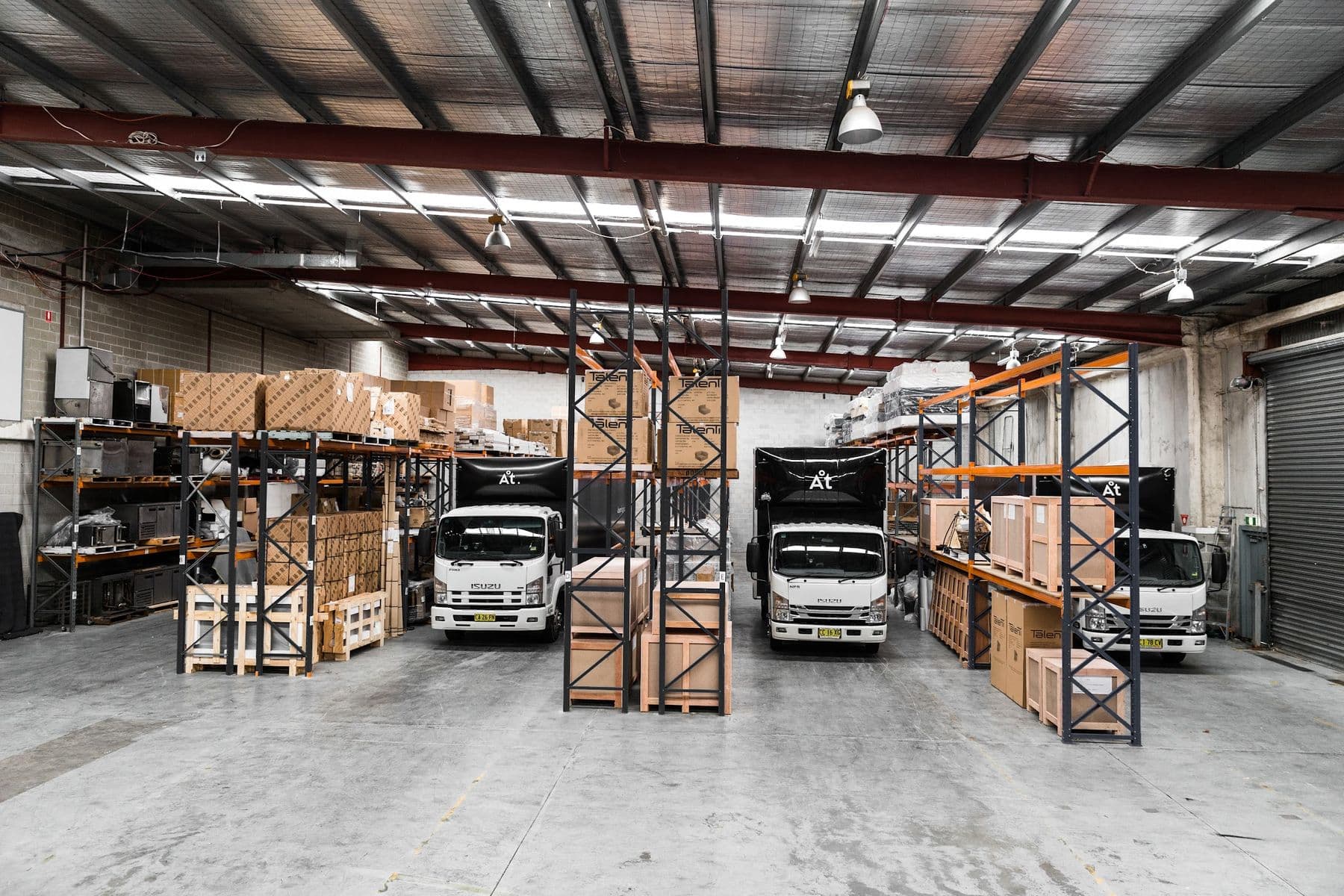 Crated stock on racking beside branded trucks at the Ateam Logistics dock.