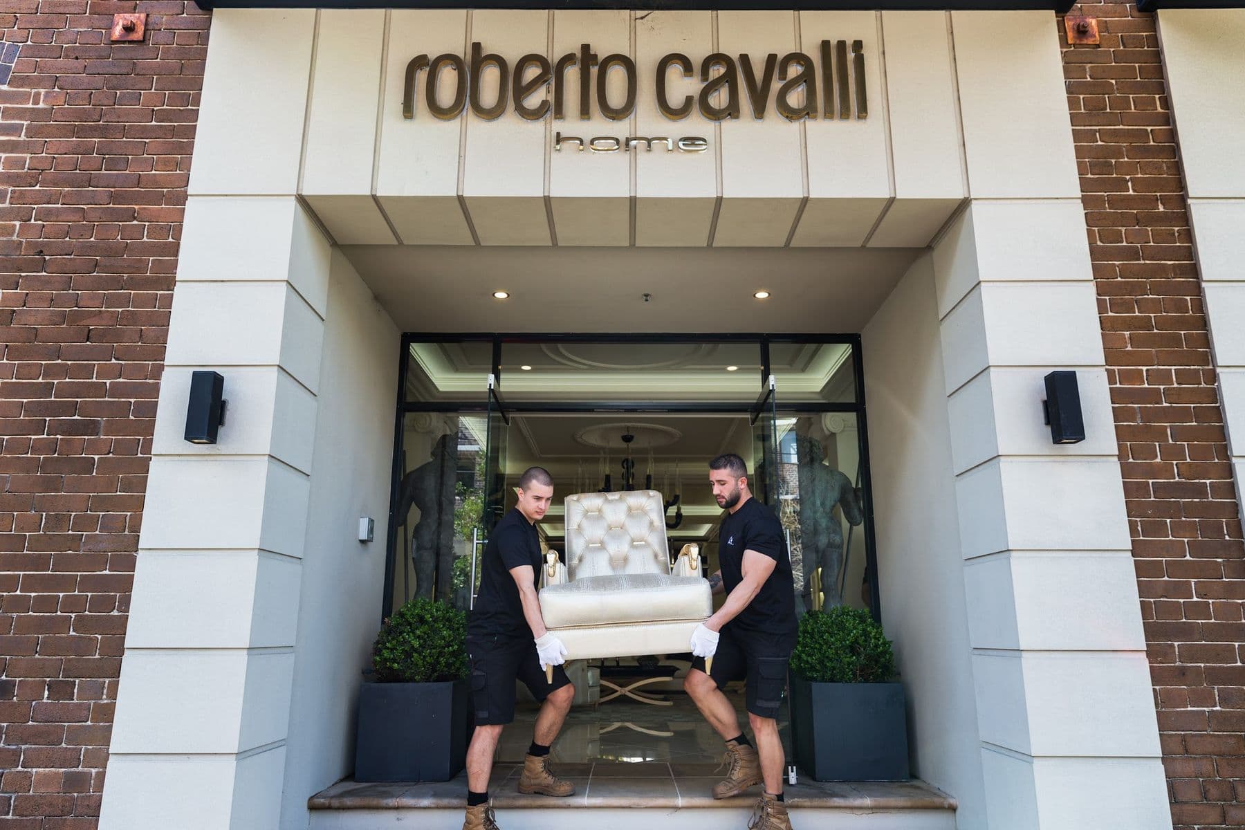 Two Ateam Logistics handlers carrying a chair out through a showroom doorway.