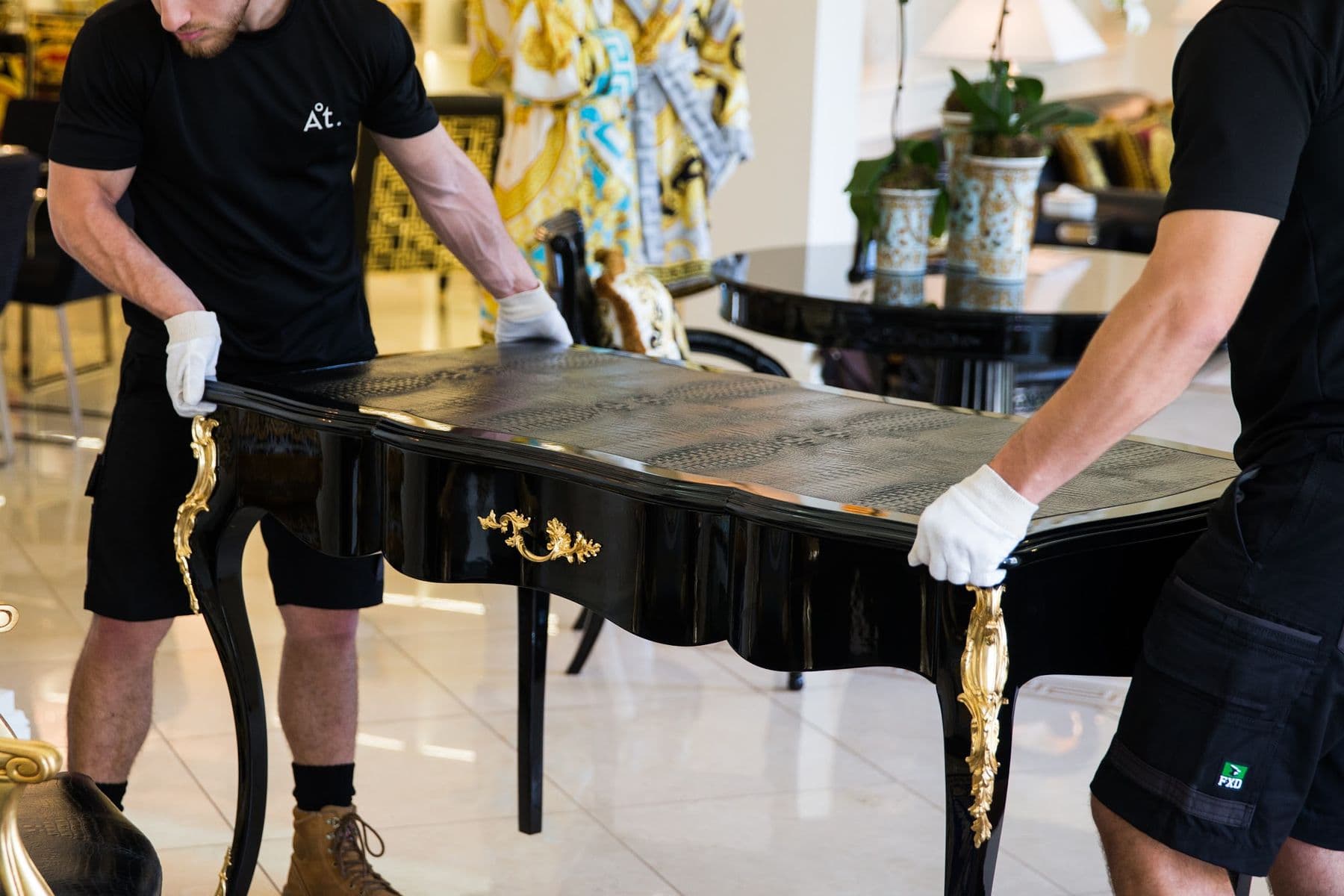 Two handlers in gloves placing a lacquered desk in position.