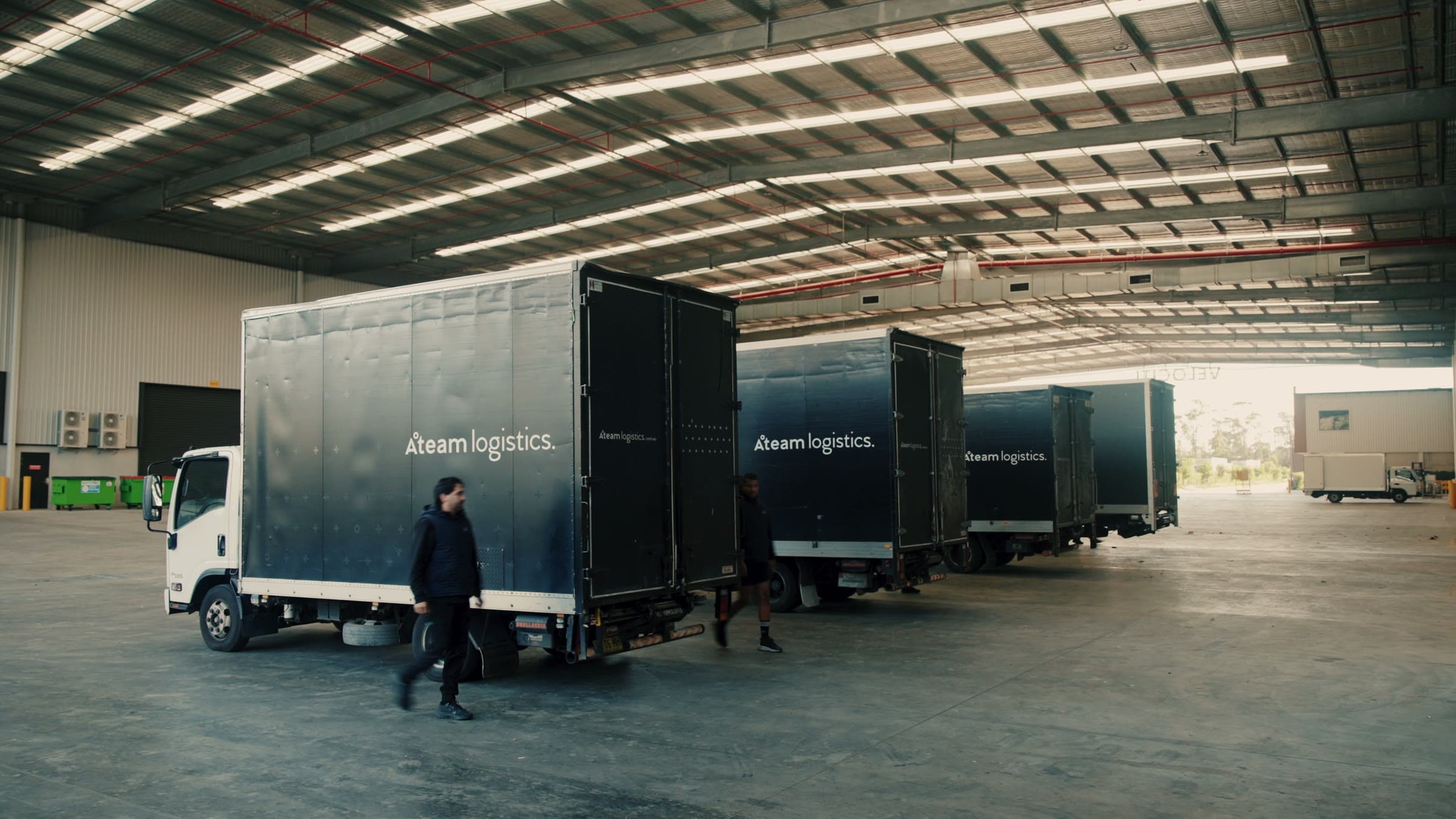 Three matte black Ateam Logistics trucks lined up at the loading docks of the Botany facility under a clear sky.
